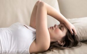 başını tutarak sırt üstü uzanmış endişeli kadın.