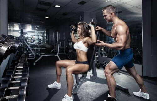 Bir erkek ve kadın birlikte military press dambıl egzersizi yapıyor.